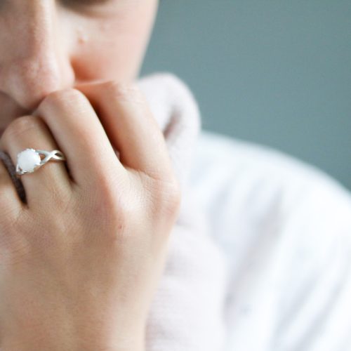 Une maman portant une bague souvenir en lait maternel, symbole précieux de l'allaitement, serrant son châle près du visage dans un moment tendre.