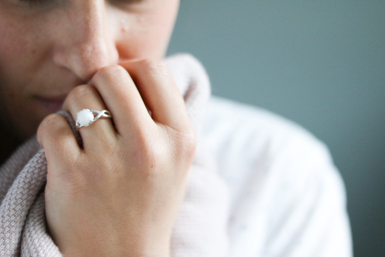 Une maman portant une bague souvenir en lait maternel, symbole précieux de l'allaitement, serrant son châle près du visage dans un moment tendre.