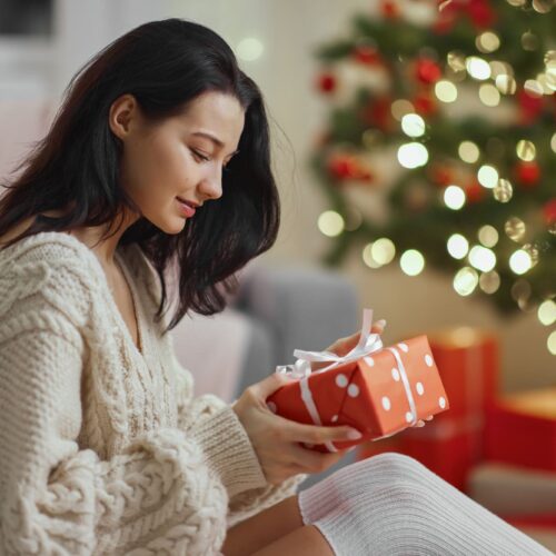 Jeune maman découvrant son cadeau de Noël devant un sapin illuminé.