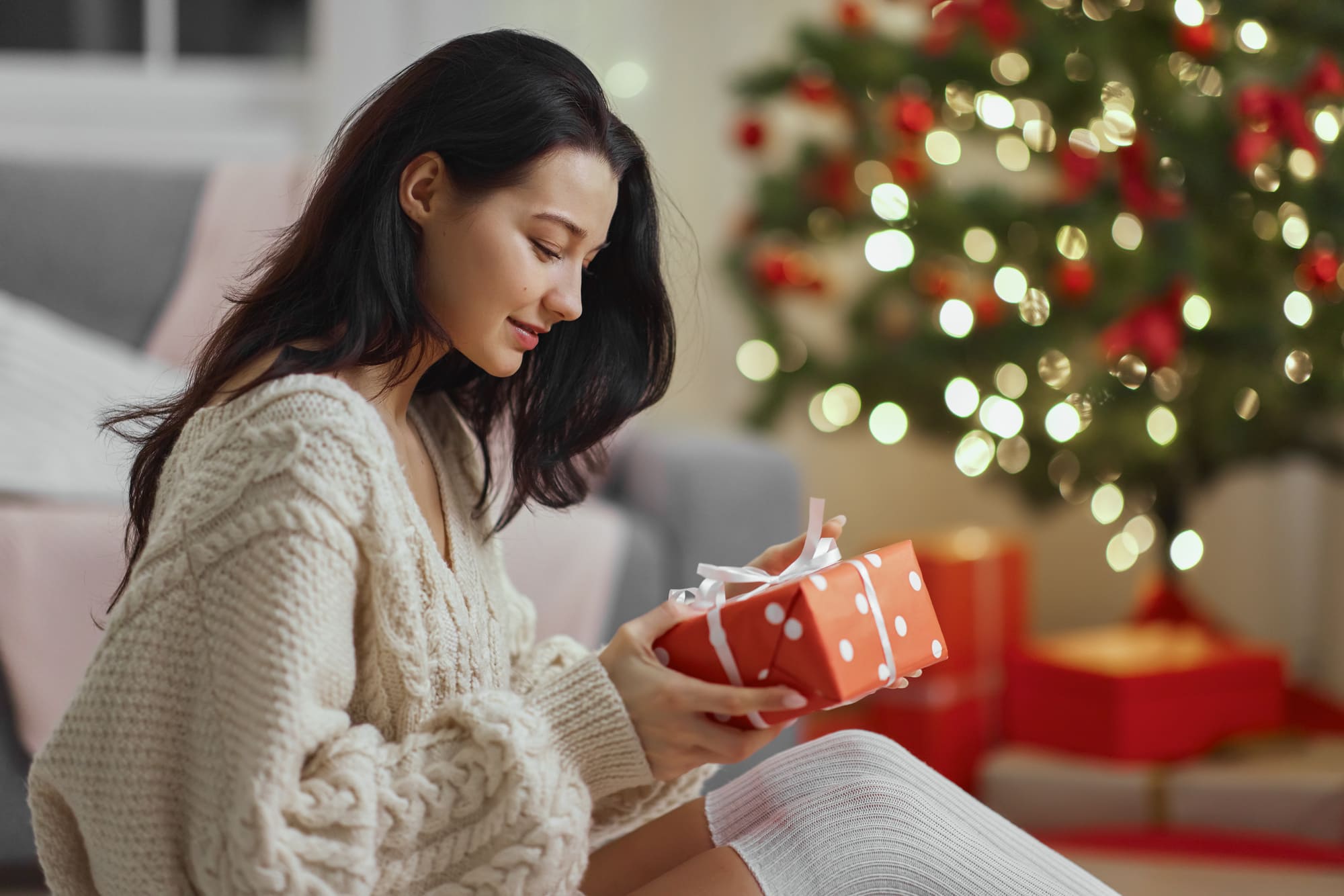 Jeune maman découvrant son cadeau de Noël devant un sapin illuminé.
