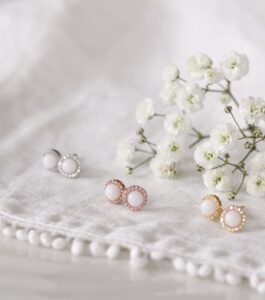 Trois paires de boucles d'oreilles en lait maternel, serties de zircons blanc, déclinées en argent, rose, et or jaune.