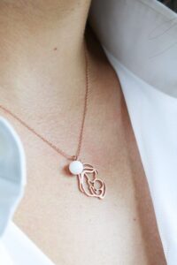 Collier en lait maternel porté au cou, avec médaille délicate en forme de silhouette de maman et bébé, symbole du lien de l'allaitement.