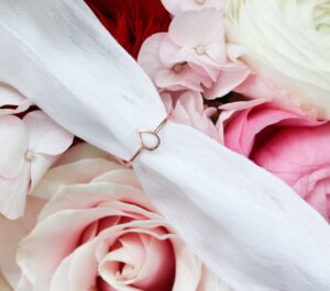 Bague en lait maternel en forme de goutte, posée sur un bouquet de rose dans les tons pâles.
