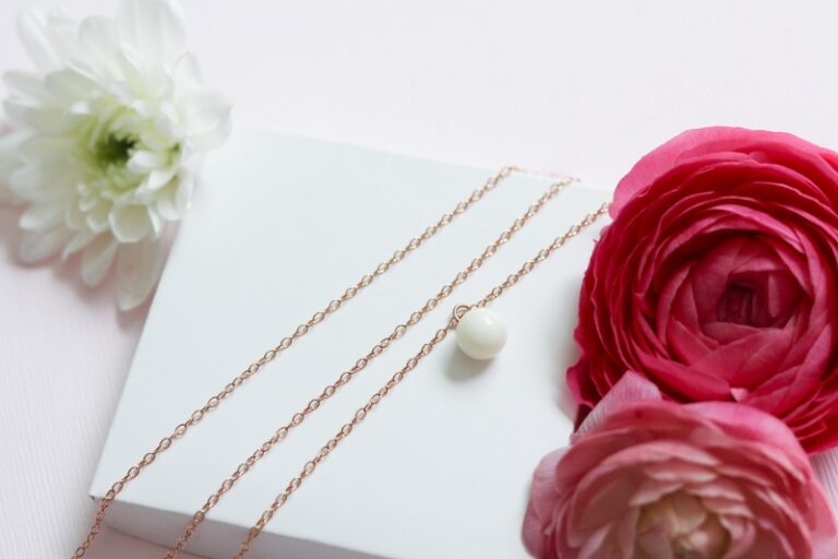 Perle de lait maternel classique présenté sur une chaine en or avec des fleurs rose en décor.