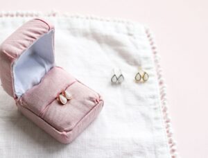 Trois paires de boucles d'oreilles en lait maternel, or jaune, or rose et argent. L'une d'elle est présentée dans un écrin rose pâle.