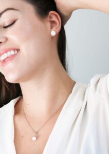 Jeune maman souriante portant des bijoux en lait maternel, boucles d'oreilles et collier, symbole précieux de son allaitement