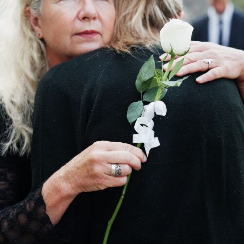 Deux femmes qui s’étreignent avec douceur, une rose blanche à la main, dans un contexte de deuil et de soutien émotionnel