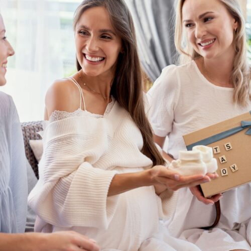 Maman d’un bébé arc-en-ciel tenant un cadeau de naissance, entourée d’autres mamans dans un moment de soutien et de douceur autour du deuil périnatal et de la maternité.